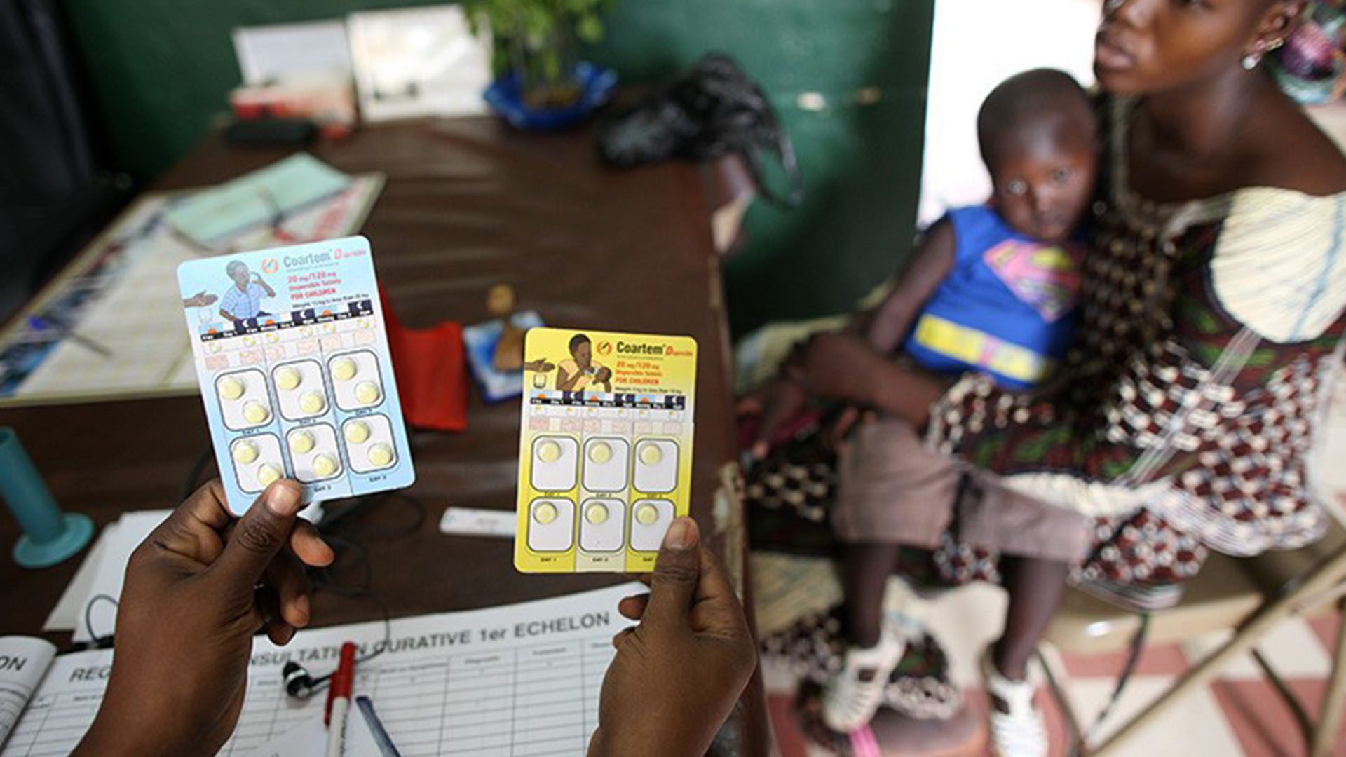 A doctor shows packets of ACT therapy to a mother and son in Mali;  Photo Credit: Godong/BSIP/Science Photo Library